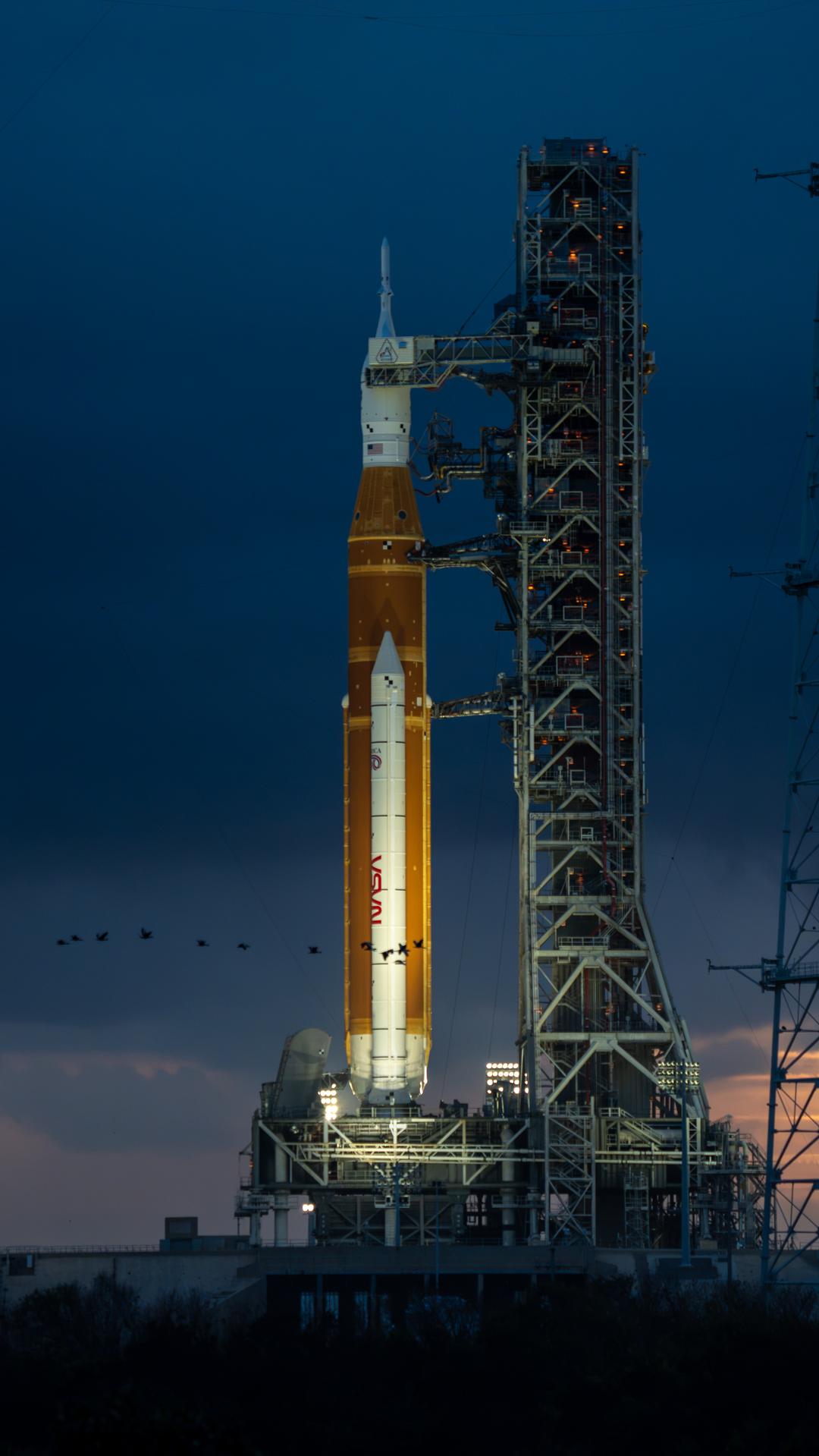 This image shows a sunset of NASA’s SLS (Space Launch System) and Orion spacecraft at NASA’s Kennedy Space Center. NASA's massive Crawler-Transporter, upgraded for the Artemis program, carried the powerful SLS rocket and Orion spacecraft on the Mobile Launcher from the Vehicle Assembly Building to Launch Pad 39B at Kennedy Space Center in preparation for the Artemis II mission.